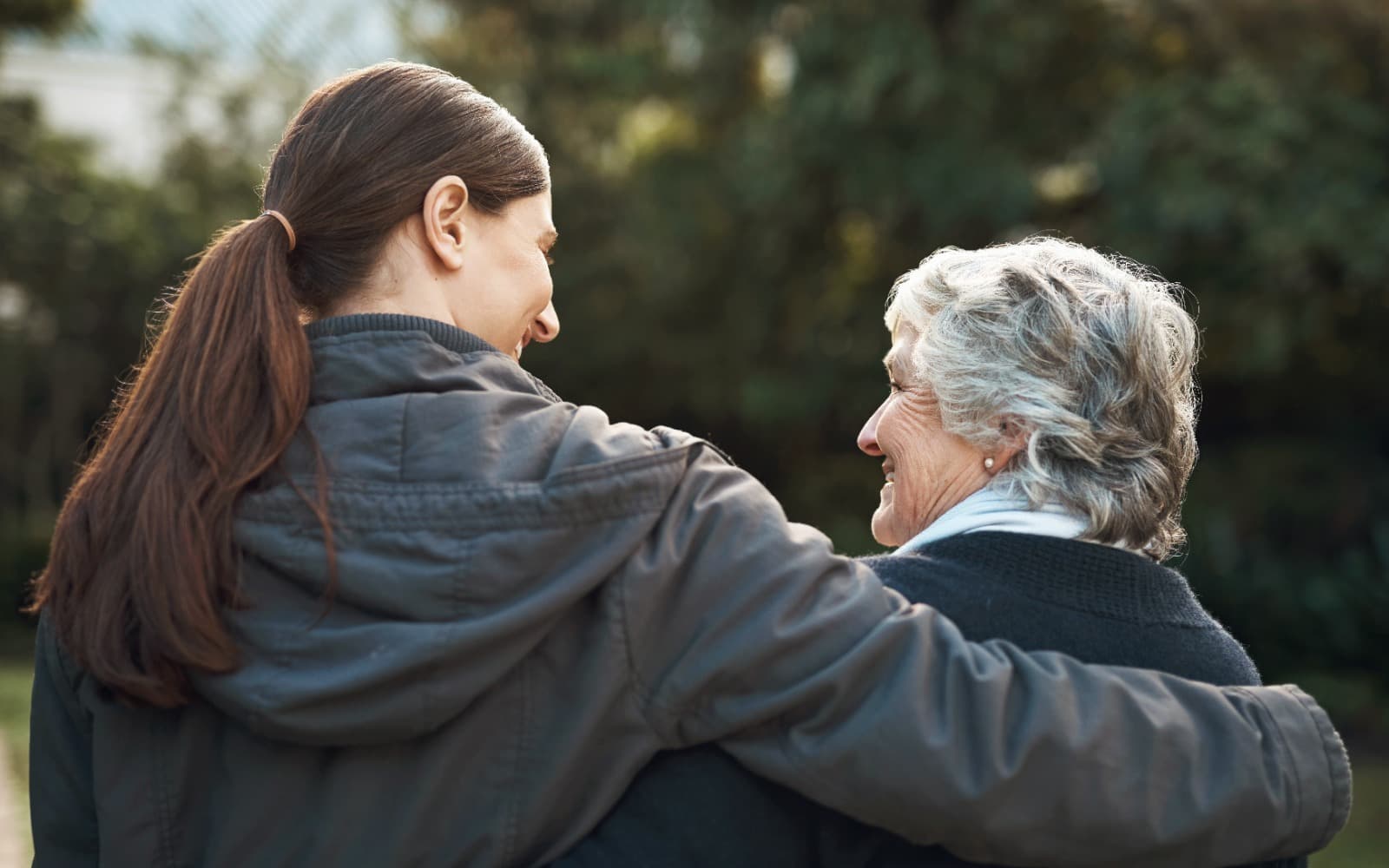 Adult daughter and older mother embracing outdoors, smiling